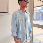 Man wearing a light blue shirt in an indoor setting with a window in the background.