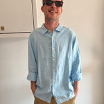 Man wearing a light blue shirt and sunglasses, standing indoors.