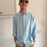Man wearing a light blue shirt and sunglasses, standing indoors.