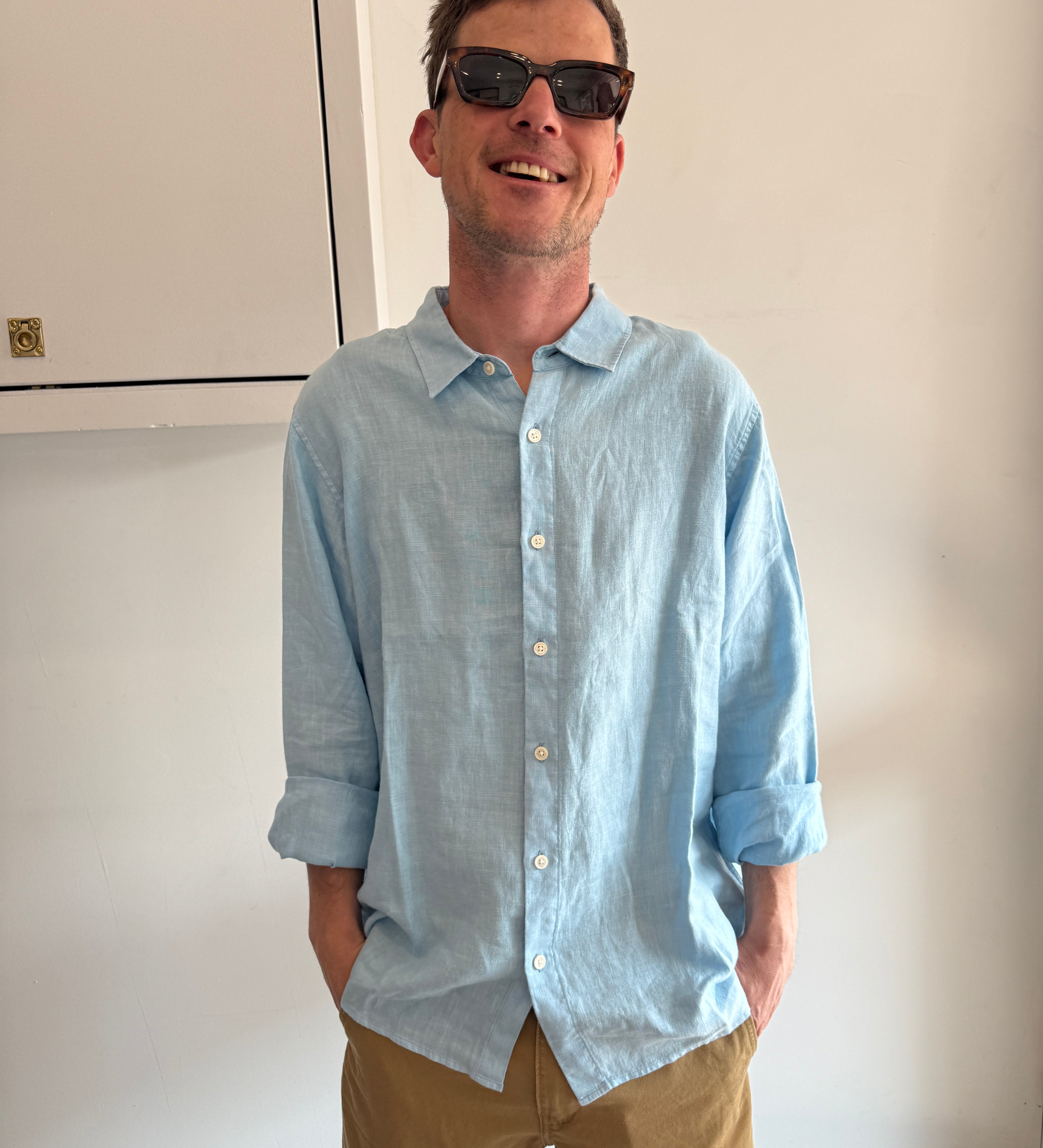 Man wearing a light blue shirt and sunglasses, standing indoors.