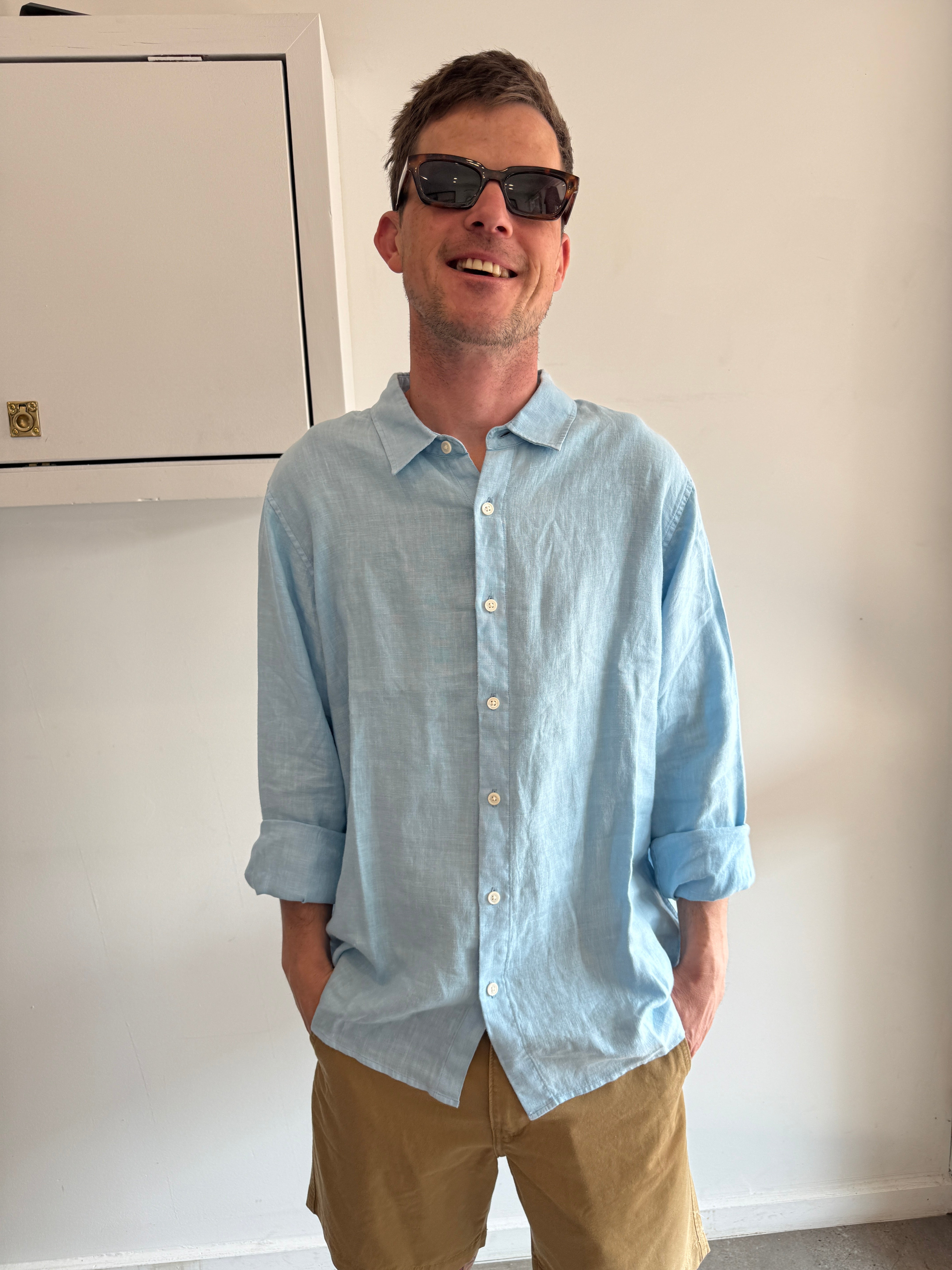 Man wearing a light blue shirt and sunglasses, standing indoors.