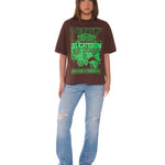 Person wearing a brown t-shirt with green text and blue jeans on a white background