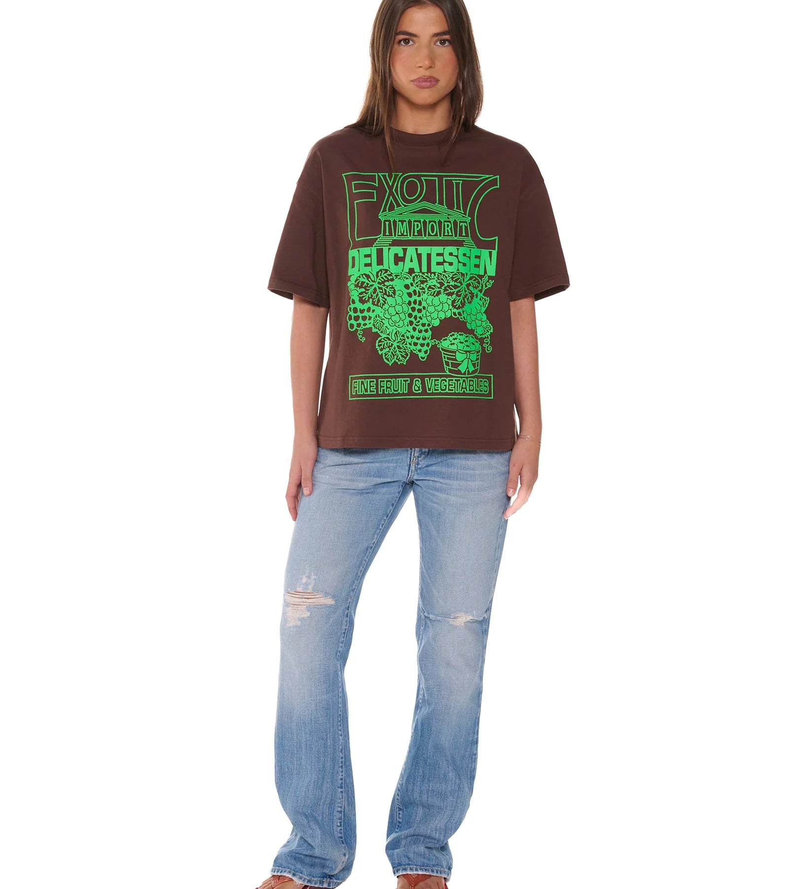 Person wearing a brown t-shirt with green text and blue jeans on a white background