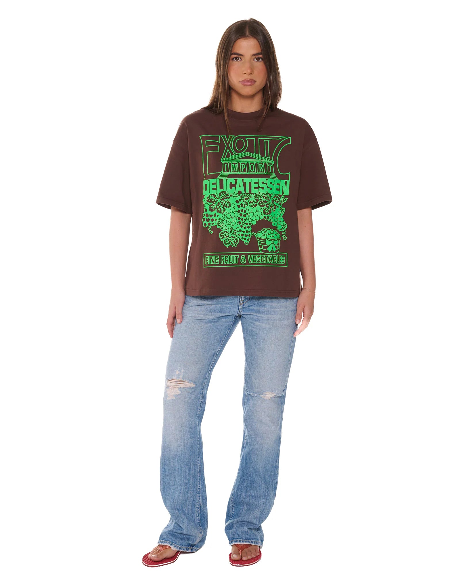 Person wearing a brown t-shirt with green text and blue jeans on a white background