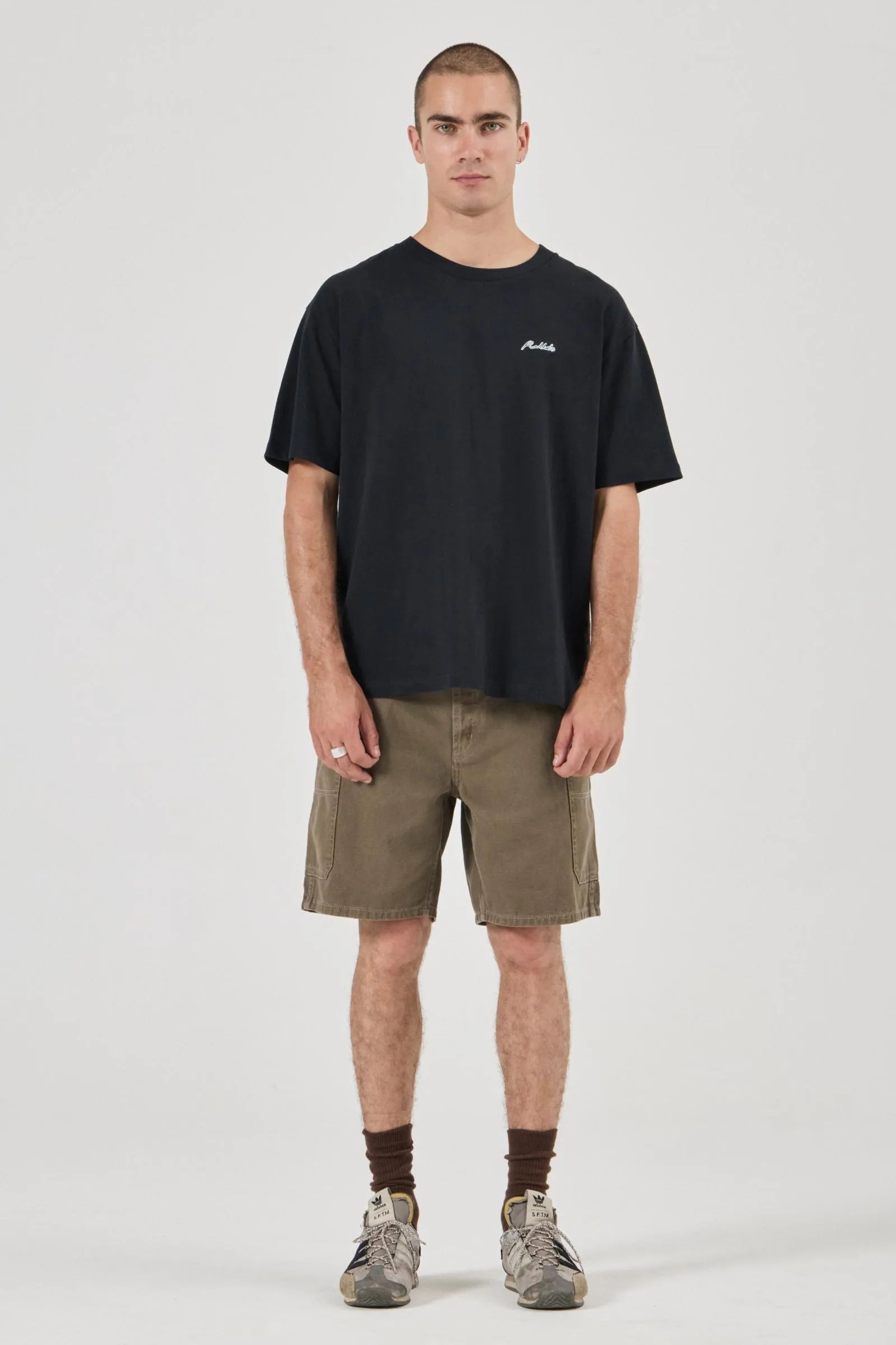 Man wearing a black t-shirt with a logo and olive shorts on a white background