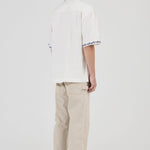 Person wearing a white shirt with text and beige pants on a white background