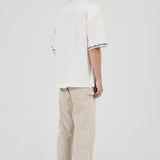 Person wearing a white shirt with text and beige pants on a white background