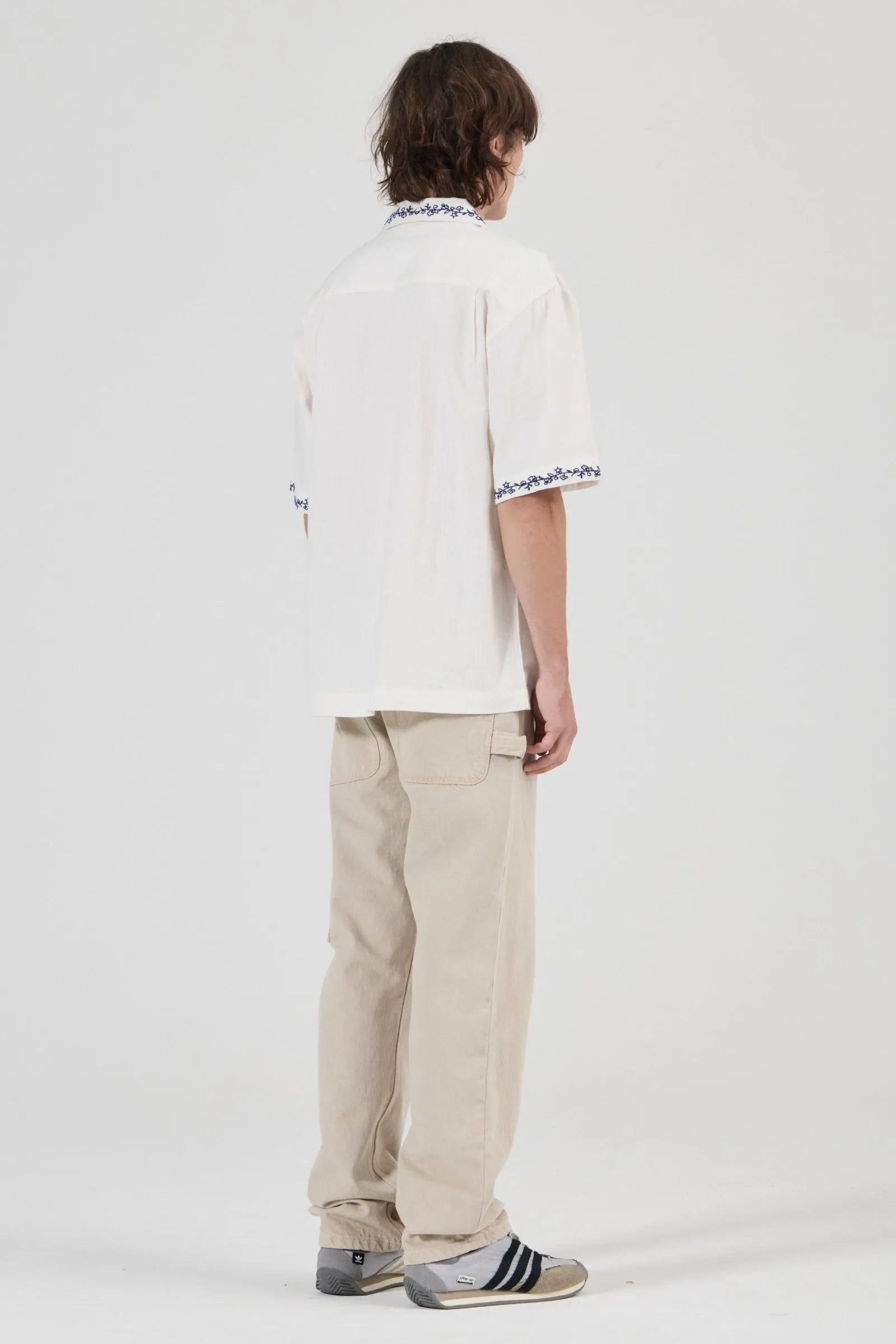 Person wearing a white shirt with text and beige pants on a white background