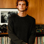Man standing in front of a record player and vinyl records on a wooden shelf.