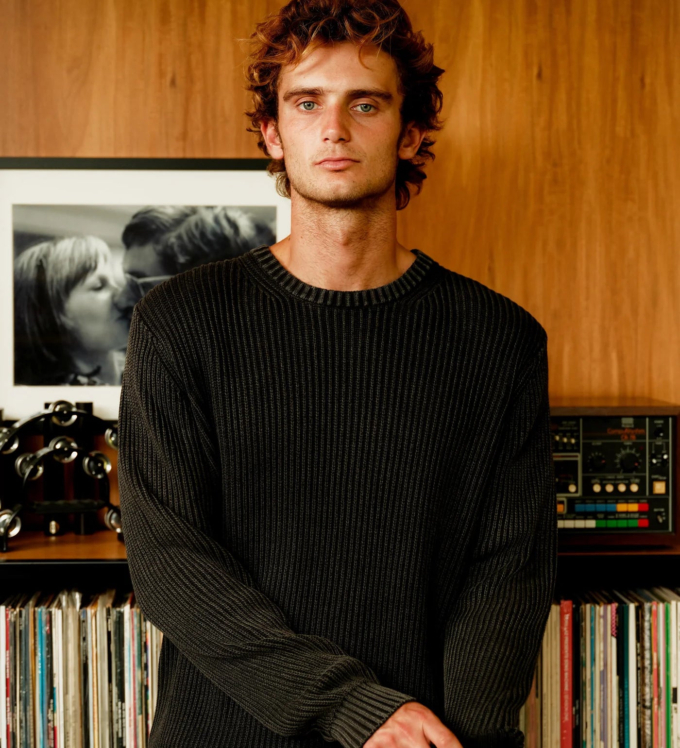 Man standing in front of a record player and vinyl records on a wooden shelf.