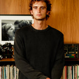 Man standing in front of a record player and vinyl records on a wooden shelf.