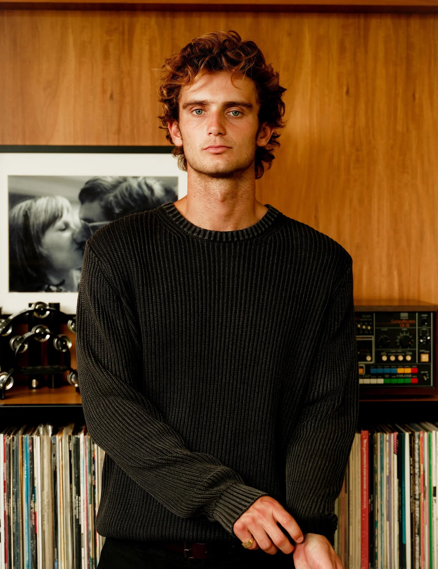 Man standing in front of a record player and vinyl records on a wooden shelf.