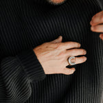 Person wearing a black ribbed sweater with a close-up of their hand and a ring.