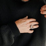 Person wearing a black ribbed sweater with a close-up of their hand and a ring.