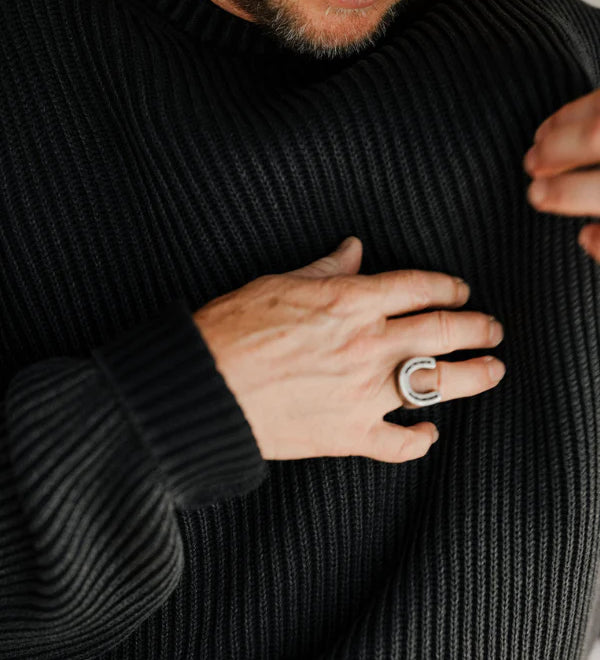 Person wearing a black ribbed sweater with a close-up of their hand and a ring.