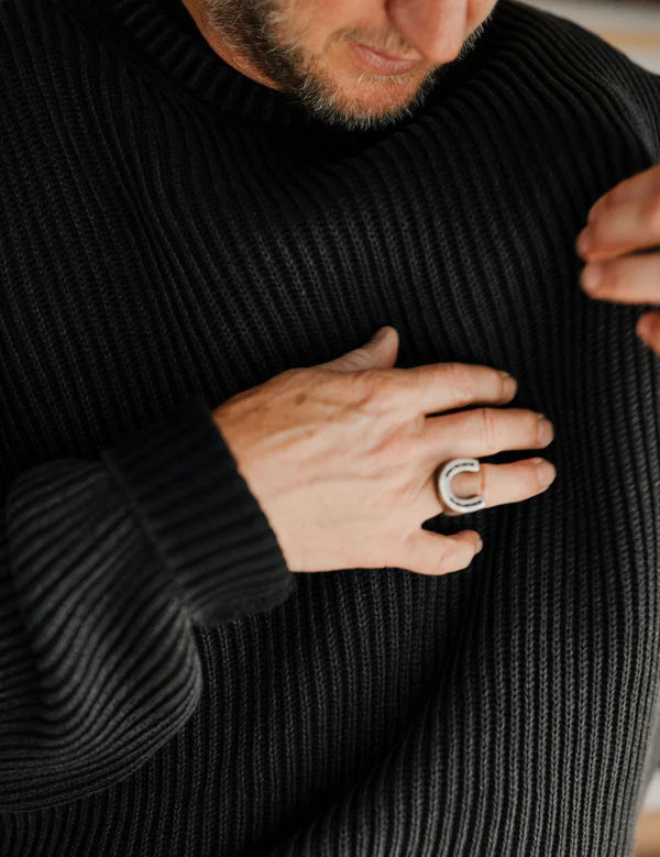 Person wearing a black ribbed sweater with a close-up of their hand and a ring.