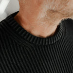 Close-up of a person wearing a black ribbed sweater with a blurred background