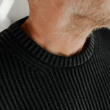 Close-up of a person wearing a black ribbed sweater with a blurred background