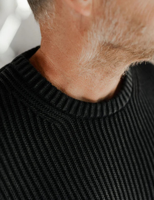 Close-up of a person wearing a black ribbed sweater with a blurred background