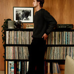 Man standing in a room with vinyl records and a photograph on a shelf.