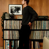 Man standing in a room with vinyl records and a photograph on a shelf.