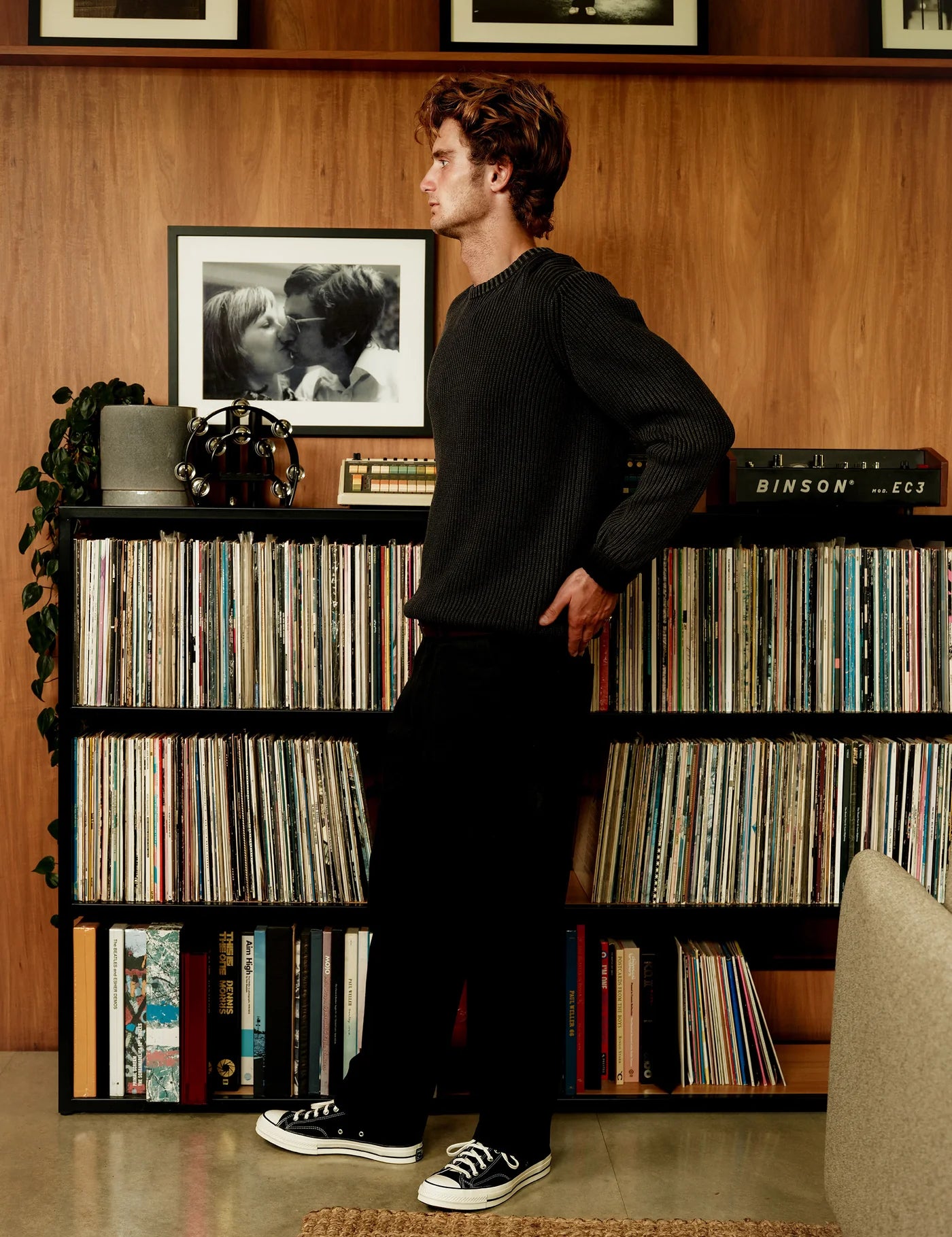 Man standing in a room with vinyl records and a photograph on a shelf.