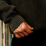 Person wearing a dark sweater holding hands with another person against a black background