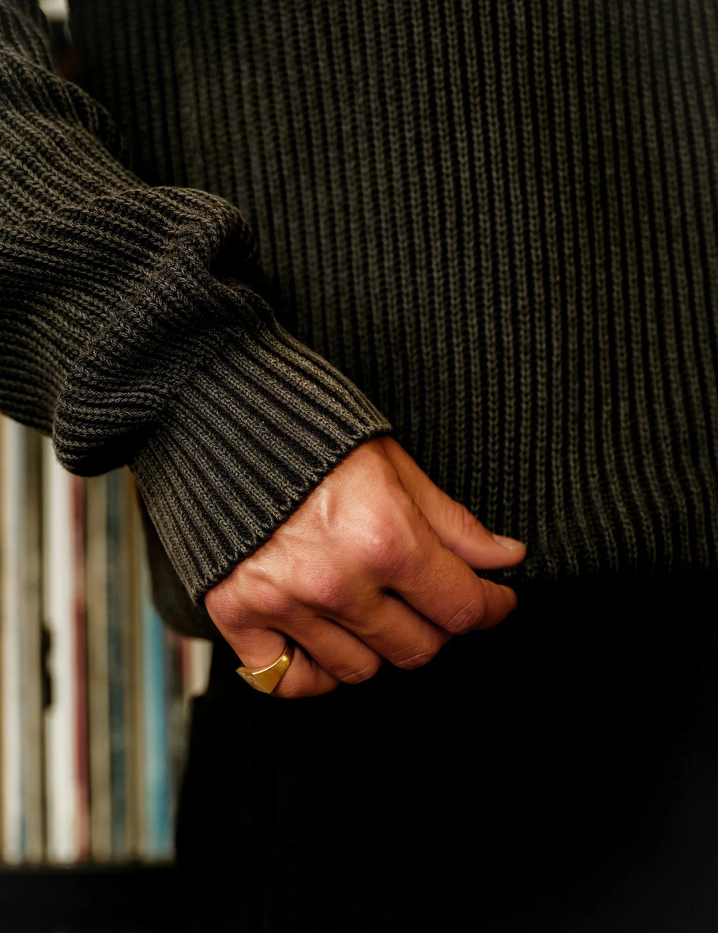 Person wearing a dark sweater holding hands with another person against a black background