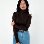 Woman wearing a brown turtleneck sweater and blue jeans on a white background