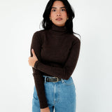 Woman wearing a brown turtleneck sweater and blue jeans on a white background