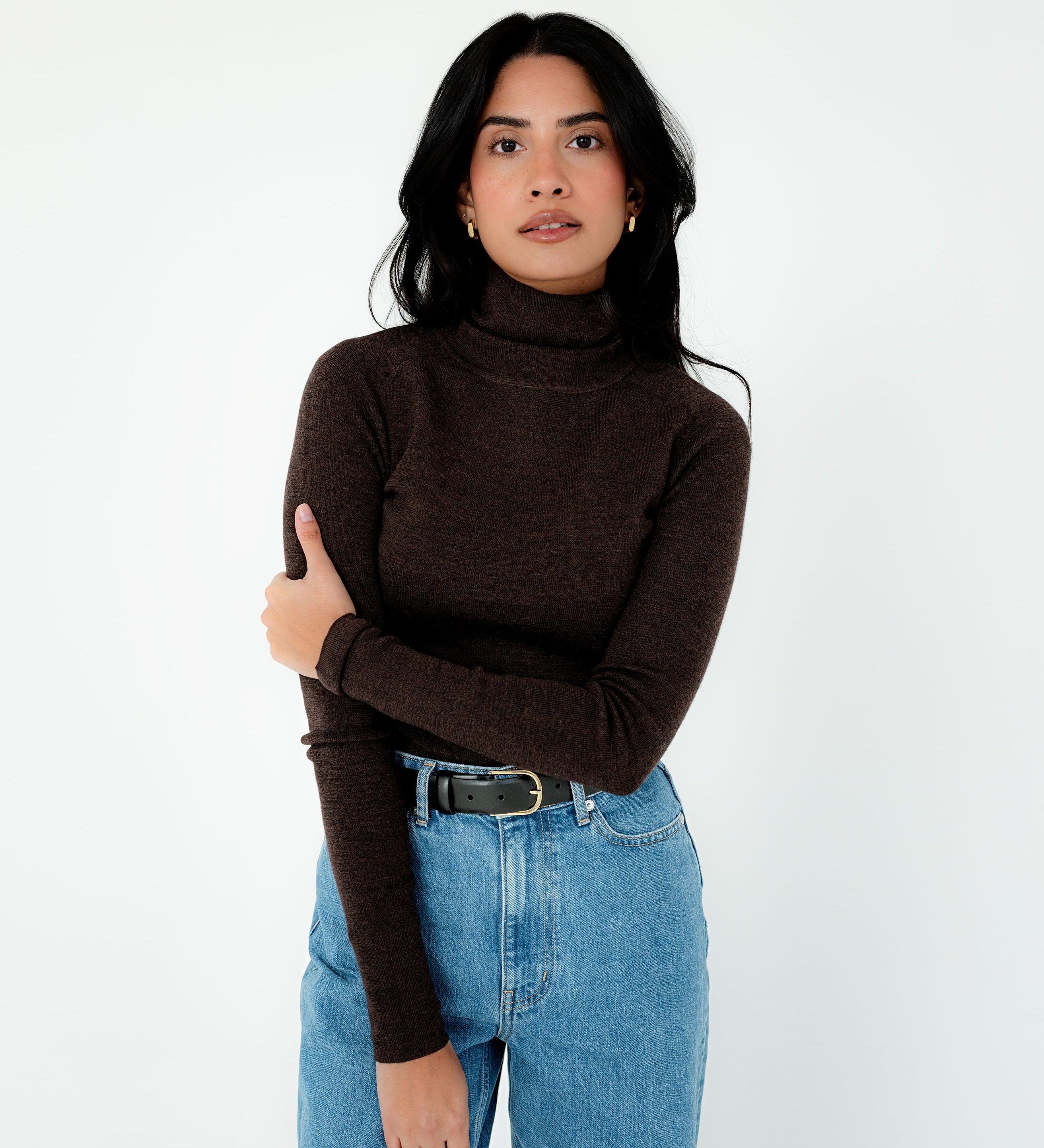 Woman wearing a brown turtleneck sweater and blue jeans on a white background