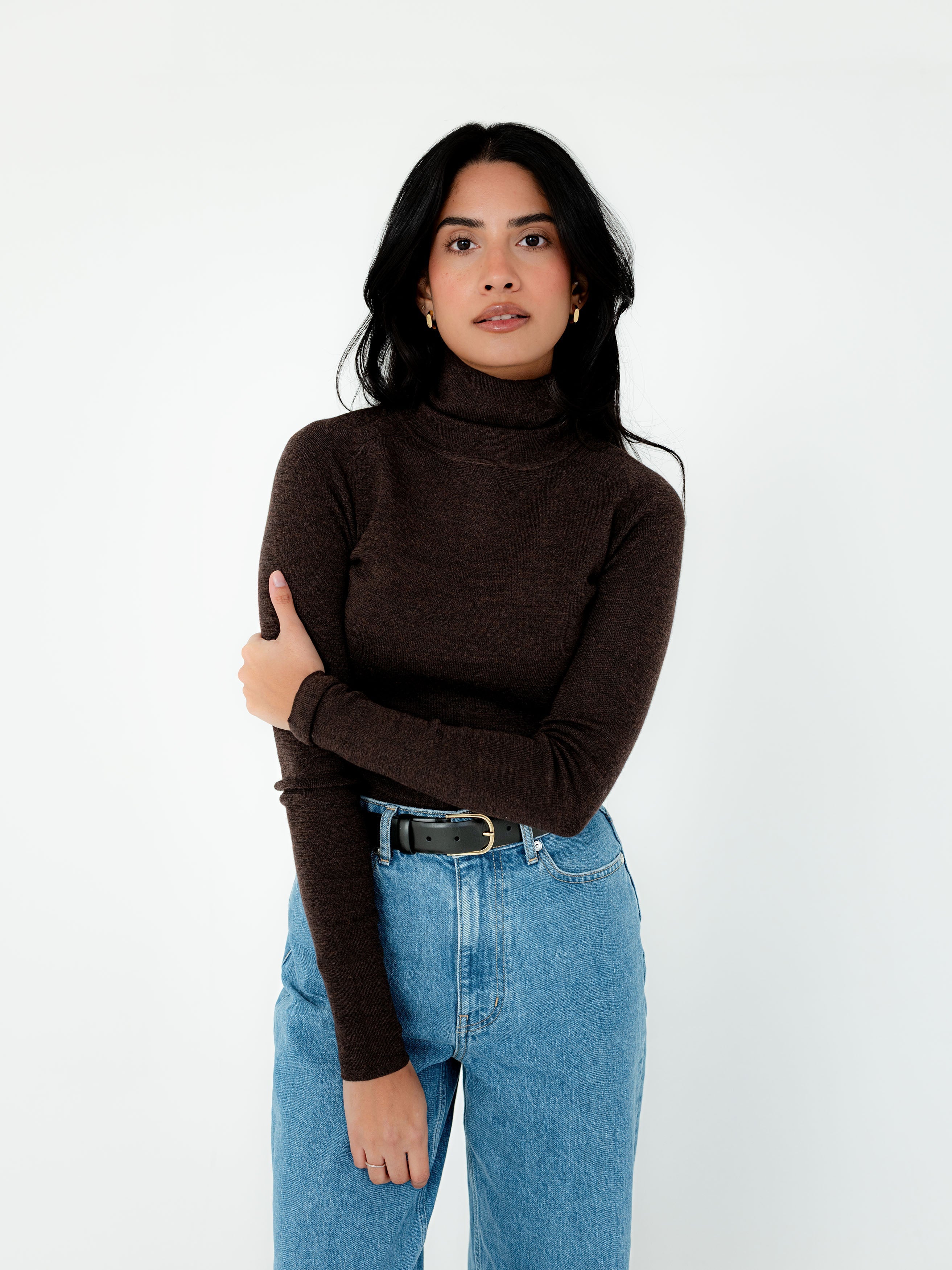 Woman wearing a brown turtleneck sweater and blue jeans on a white background