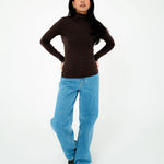 Person wearing a brown turtleneck and blue jeans on a white background