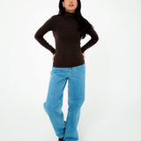 Person wearing a brown turtleneck and blue jeans on a white background