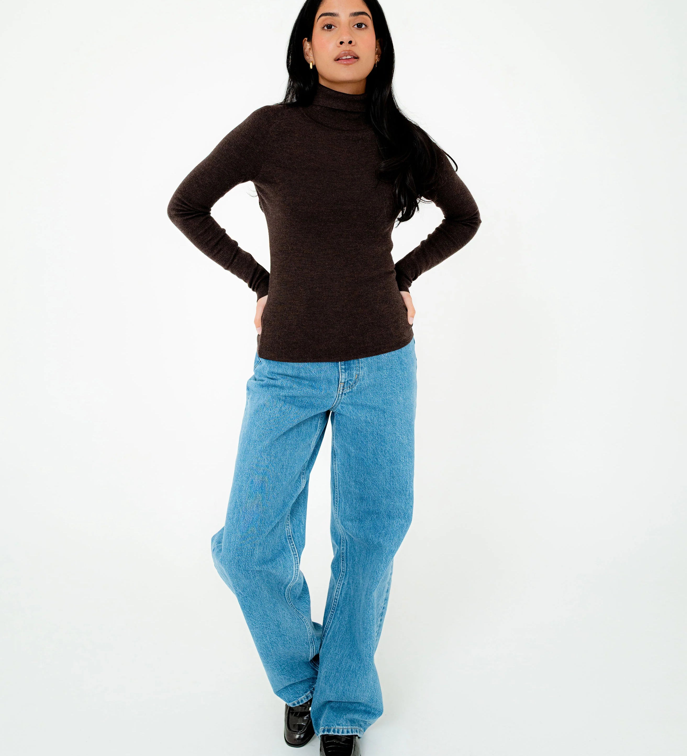 Person wearing a brown turtleneck and blue jeans on a white background