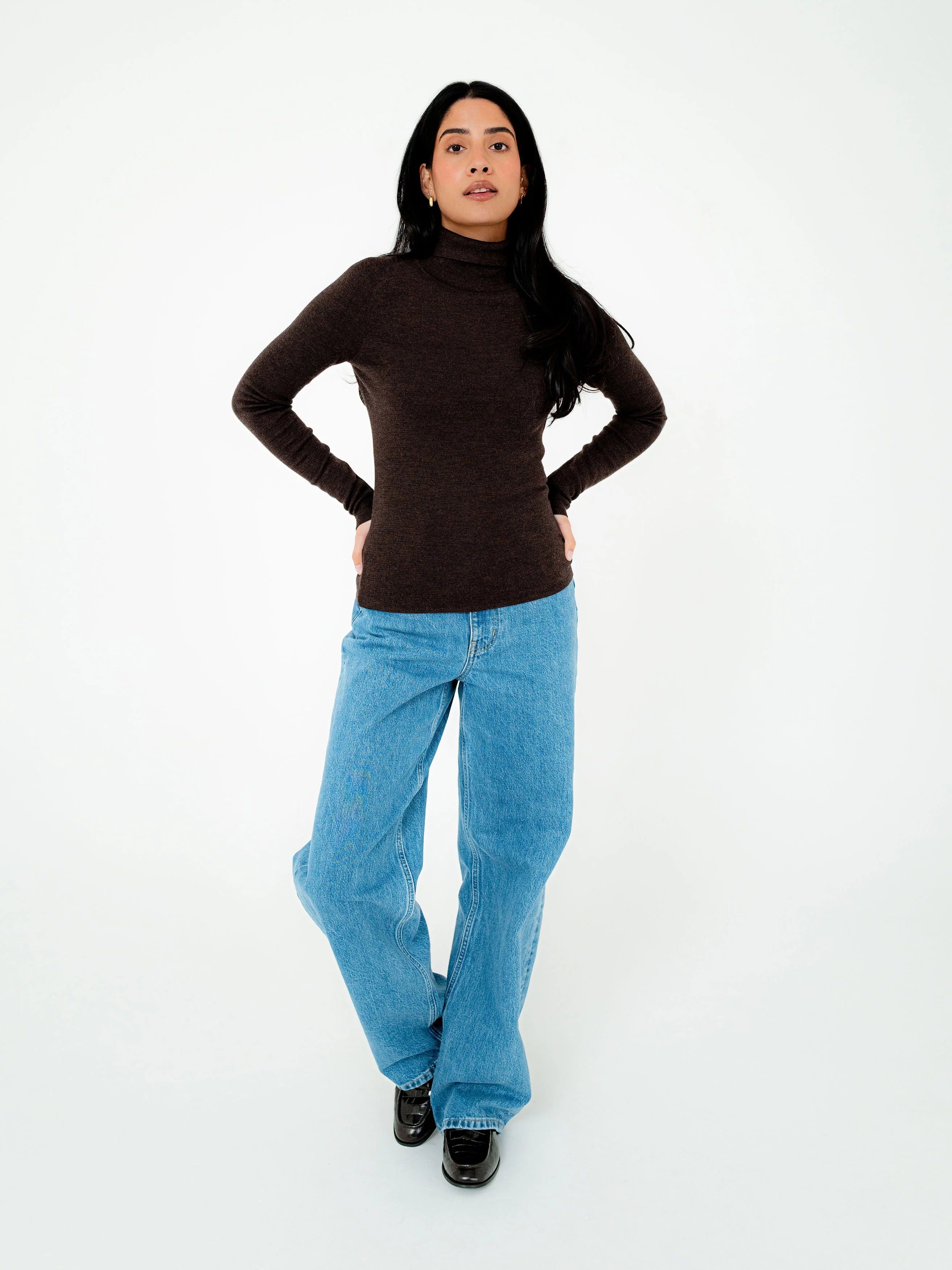 Person wearing a brown turtleneck and blue jeans on a white background