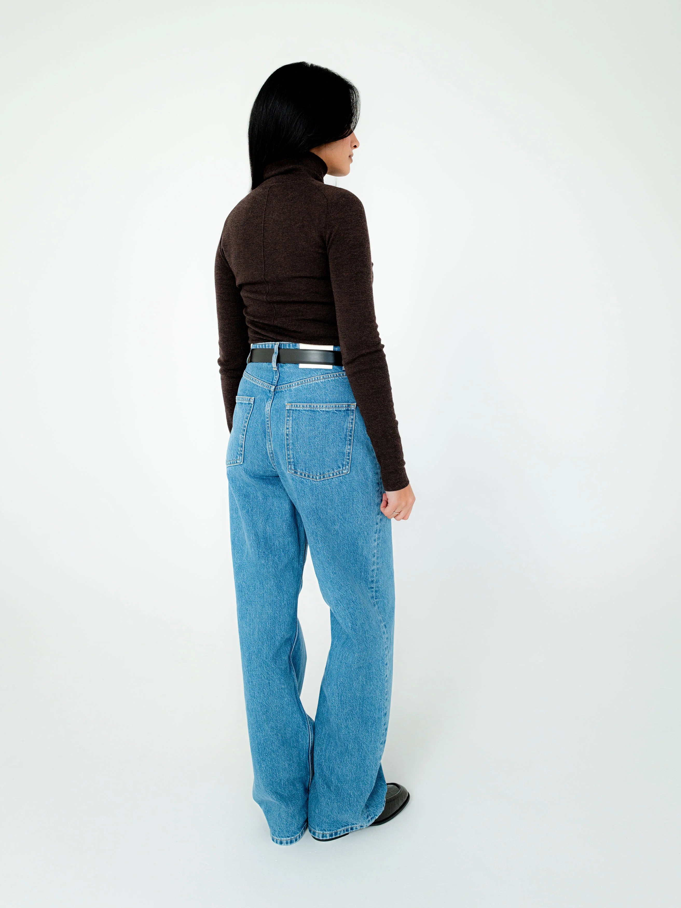 Person wearing blue jeans and a brown top on a white background