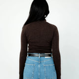 Person wearing a brown long-sleeve top and blue jeans from behind on a white background