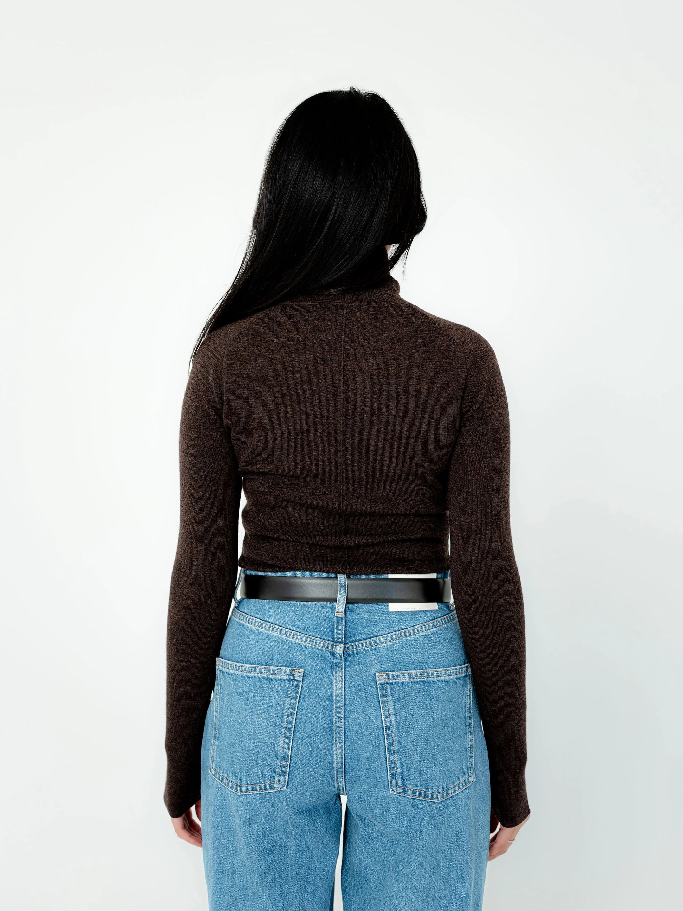 Person wearing a brown long-sleeve top and blue jeans from behind on a white background