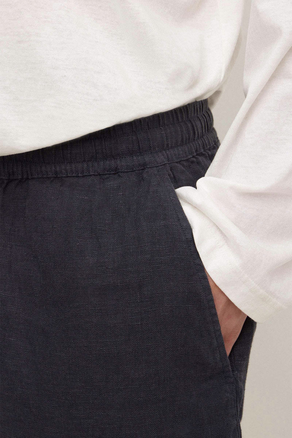 Close-up of a person wearing dark charcoal gray linen trousers with an elastic waistband and a white long-sleeve top.