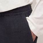 Close-up of a person wearing dark charcoal gray linen trousers with an elastic waistband and a white long-sleeve top.