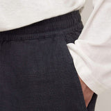 Close-up of a person wearing dark charcoal gray linen trousers with an elastic waistband and a white long-sleeve top.