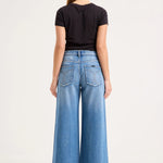 A woman viewed from the back wearing a black short-sleeve t-shirt and high-waisted, wide-leg blue denim jeans against a plain white studio background.