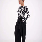 Person wearing a black and white zebra-striped shirt with wide-leg black pants on a white background