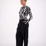 Person wearing a black and white zebra-striped shirt with wide-leg black pants on a white background