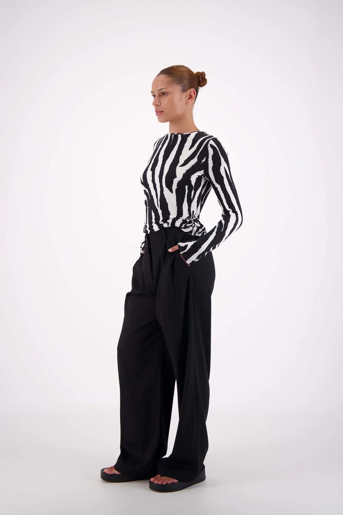 Person wearing a black and white zebra-striped shirt with wide-leg black pants on a white background