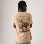 A man shown from behind wearing a beige t-shirt with a large brown graphic print on the back, paired with blue jeans, against a plain light gray background.