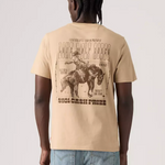 A man viewed from behind wearing a beige graphic t-shirt with a large western-themed print on the back, paired with light blue jeans, against a light gray studio background.