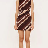 A woman modeling a sleeveless bodycon mini dress with a brown and beige tie-dye pattern, standing against a plain off-white background.