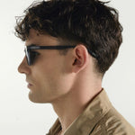 Man wearing sunglasses and a brown jacket against a white background